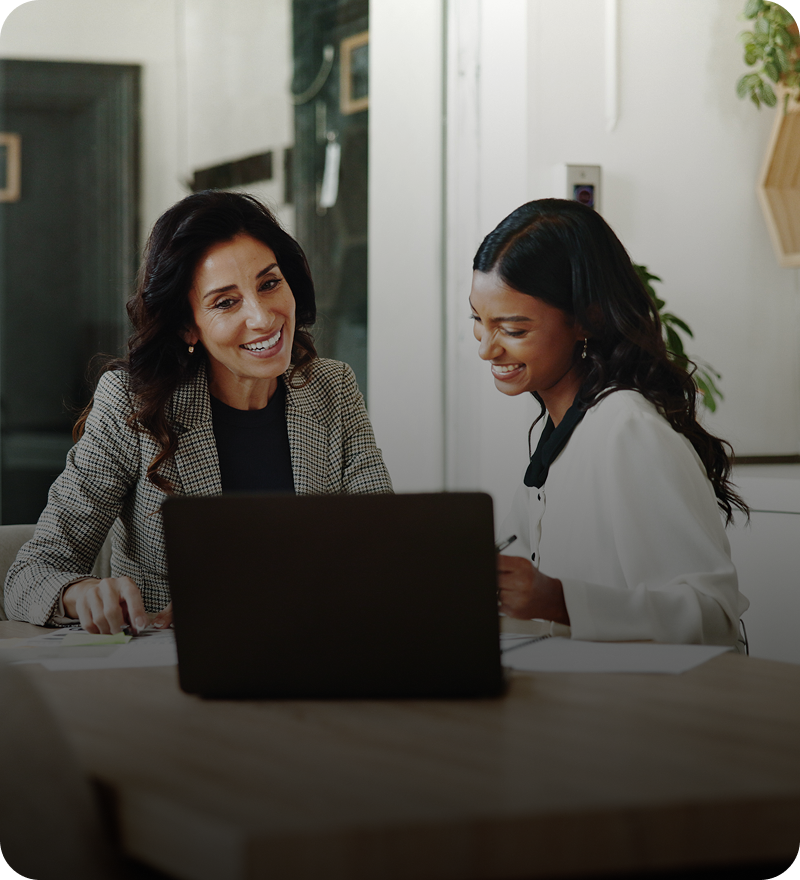 Two women smiling at a laptop screen.